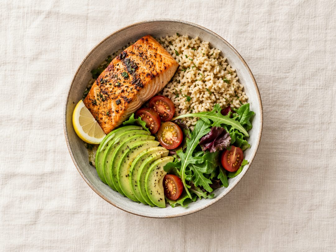 Overhead view of a bowl with salmon, brown rice, avocado and greens
